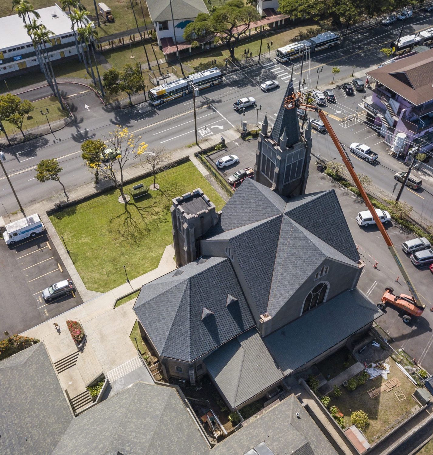 Aerial view of a gray church with a tall steeple, surrounded by a street with cars and buses.