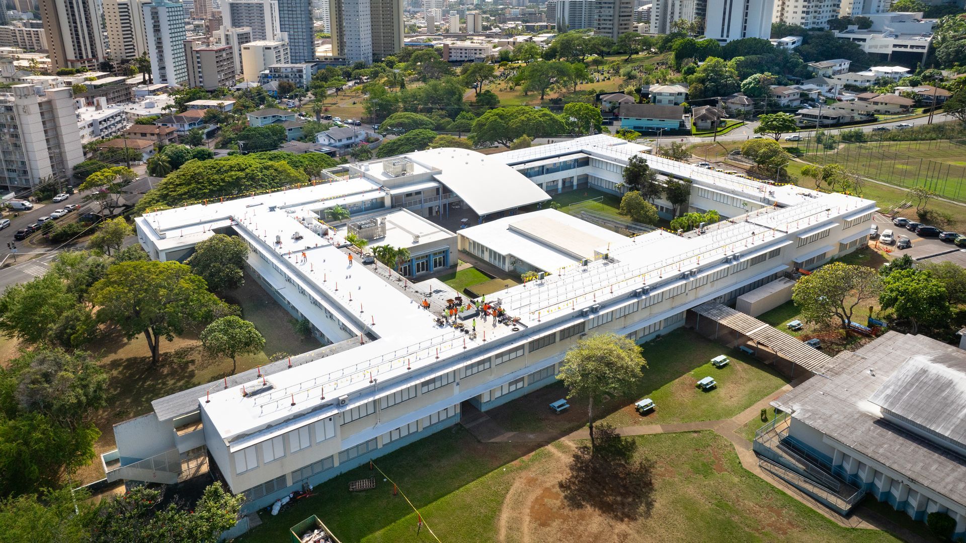 Aerial view of a large, white building with a central courtyard and surrounding green space, likely a school.