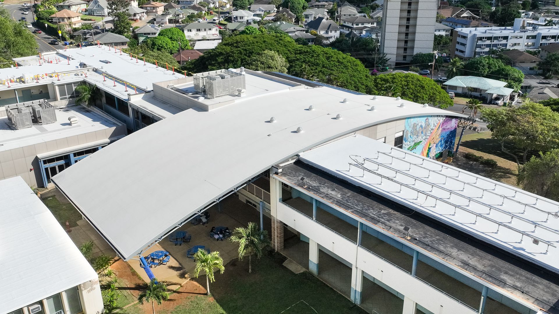 Aerial view of a school building with a curved white roof, surrounded by trees and other buildings.