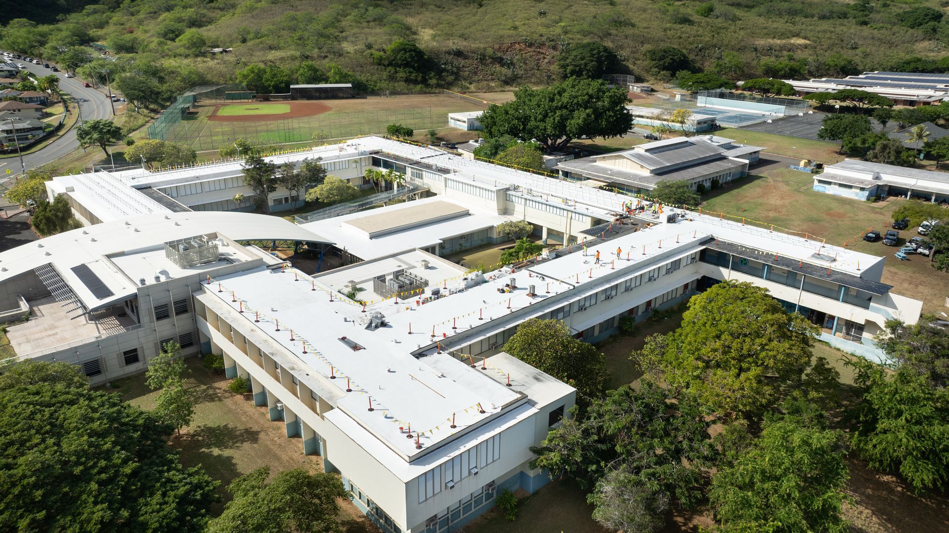 Aerial view of a white, multi-building structure with a courtyard, surrounded by trees and a hillside.