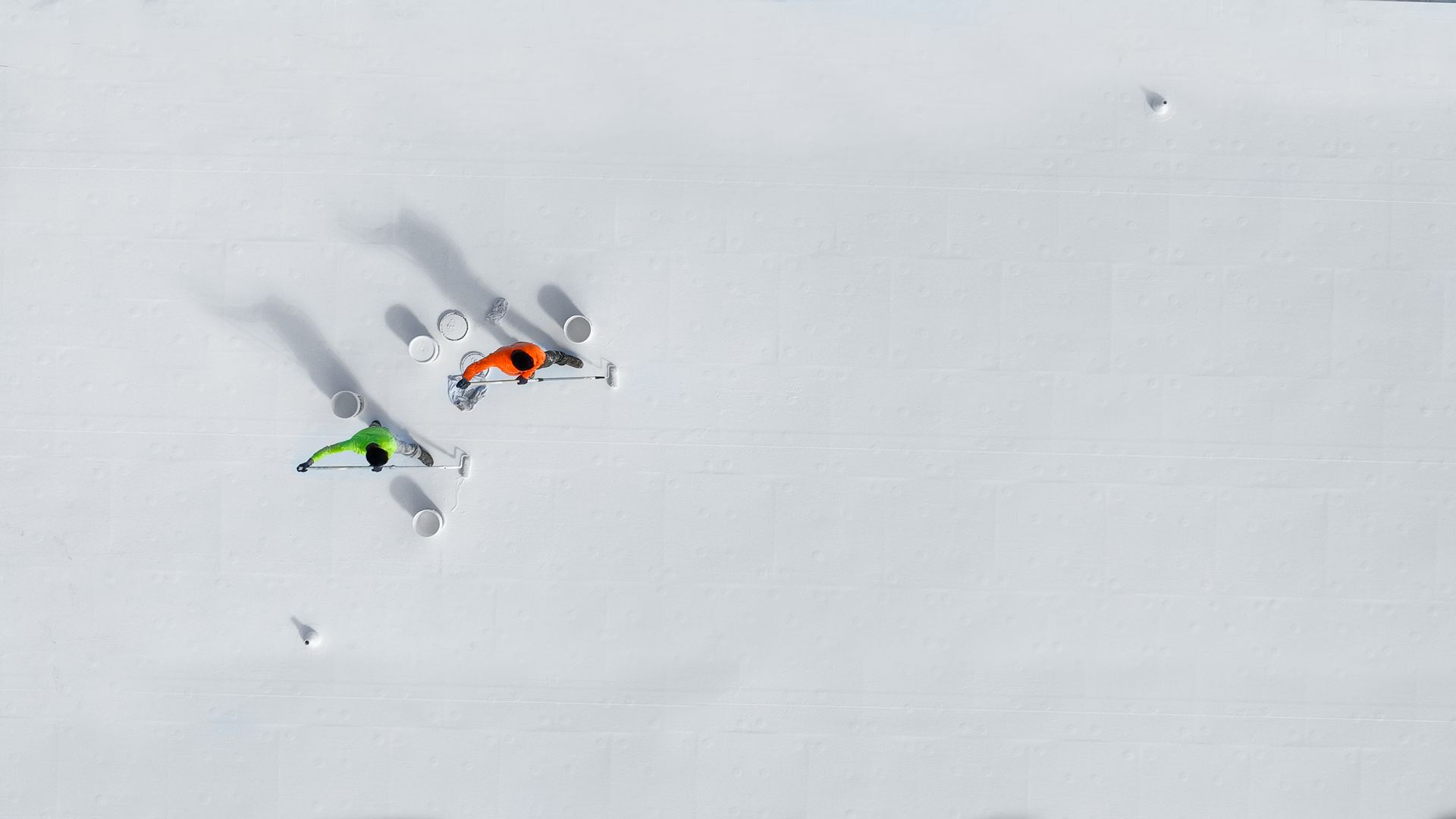 Two skiers on a snowy slope, one in green, the other orange, viewed from above.