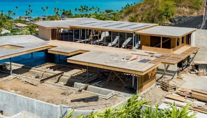 House under construction on a hillside overlooking the ocean; wood framing visible.