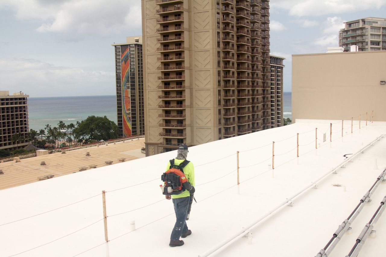 Worker on white rooftop, walking toward ocean view between tall buildings.