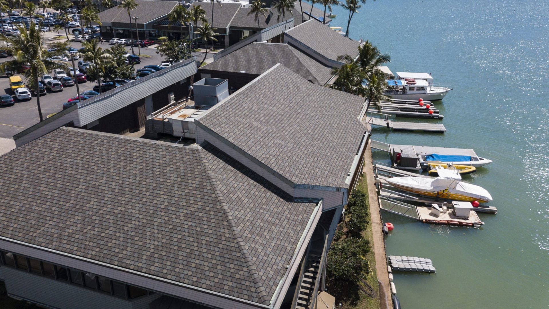 Aerial view of a building with a gray roof next to a body of water and boats.