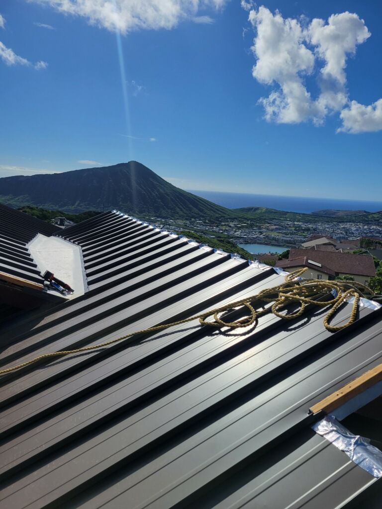 Dark metal roof with rope, mountain and ocean view under a sunny blue sky.