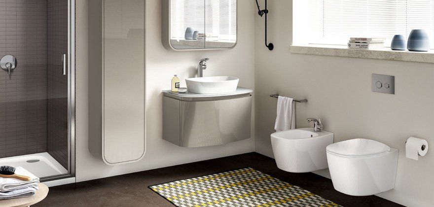 Bagno moderno con doccia, lavandino sospeso e WC, con un tappeto colorato.