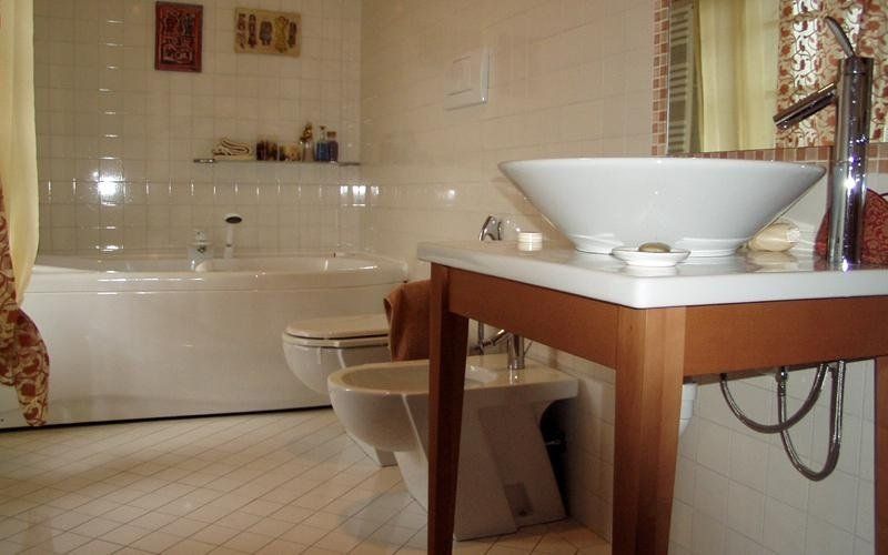 Bagno con sanitari bianchi, tra cui lavandino, WC, bidet e vasca, su uno sfondo di pareti bianche e di colore chiaro.