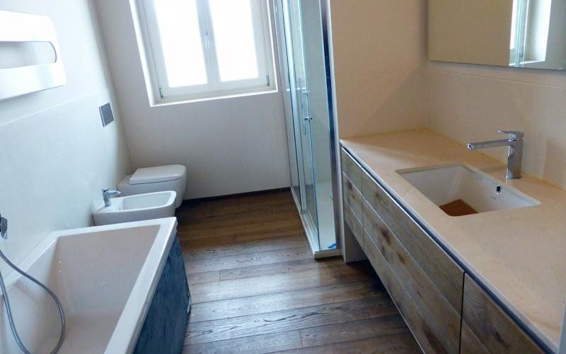 Bagno con pavimento in legno, sanitari bianchi: vasca, WC, bidet e lavandino. Doccia e finestra presenti.