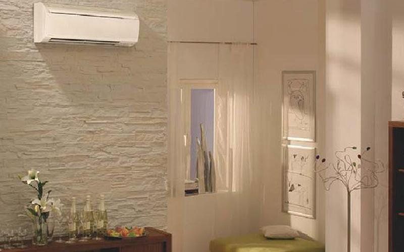 Condizionatore d'aria montato su una parete bianca ruvida in un soggiorno con finestra e tende trasparenti.