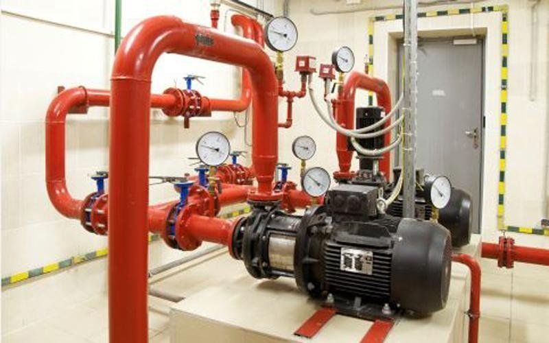 Sistema di pompa antincendio rossa con manometri e valvole in un locale tecnico.