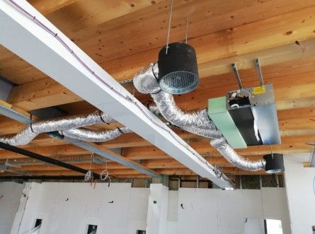 Sistema HVAC installato su un soffitto in legno con condotti argentati e bocchette circolari nere.