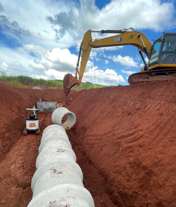 Uma escavadeira coloca tubos de concreto em uma vala em um canteiro de obras.