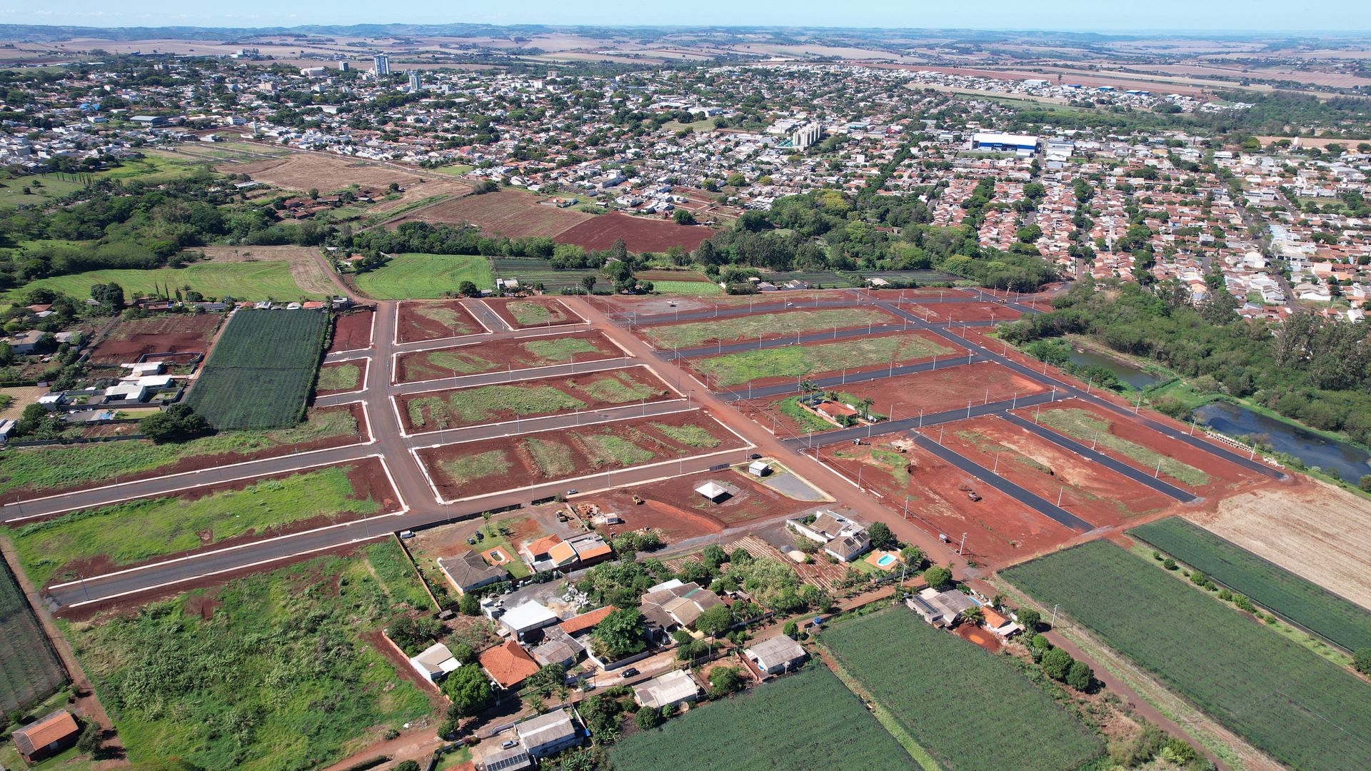 Vista aérea de uma cidade com terrenos agrícolas de solo vermelho e um rio.