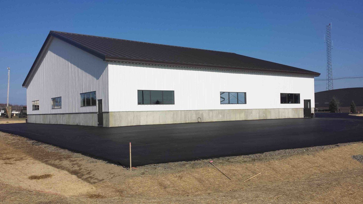 A large white building with a black roof is sitting on top of a dirt field.