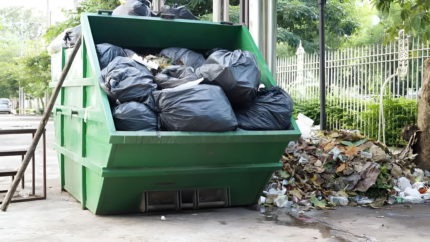 Green Dumpster Overflowing With Black Trash Bags
