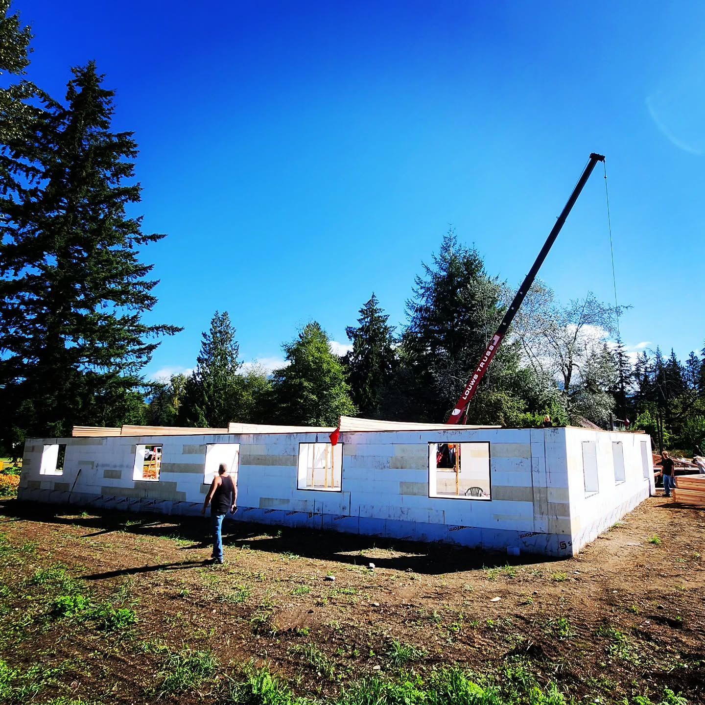 Construction of a white house with a crane on a sunny day. A person stands nearby.