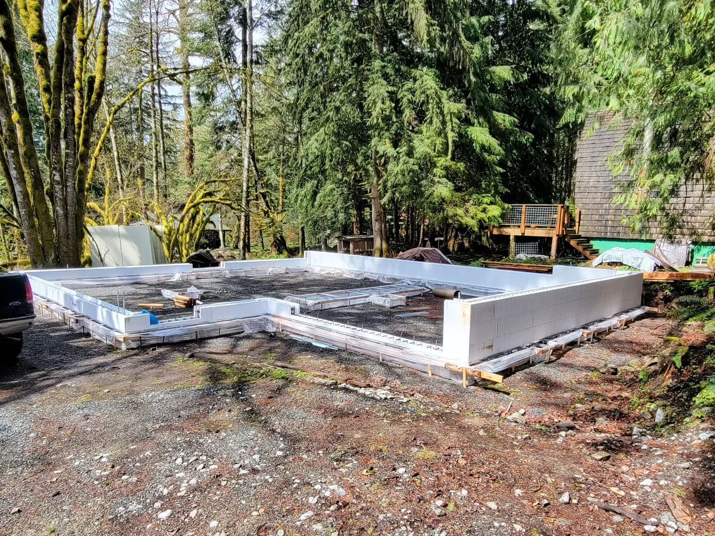 Foundation forms made of white blocks, set on gravel, in a wooded outdoor area.