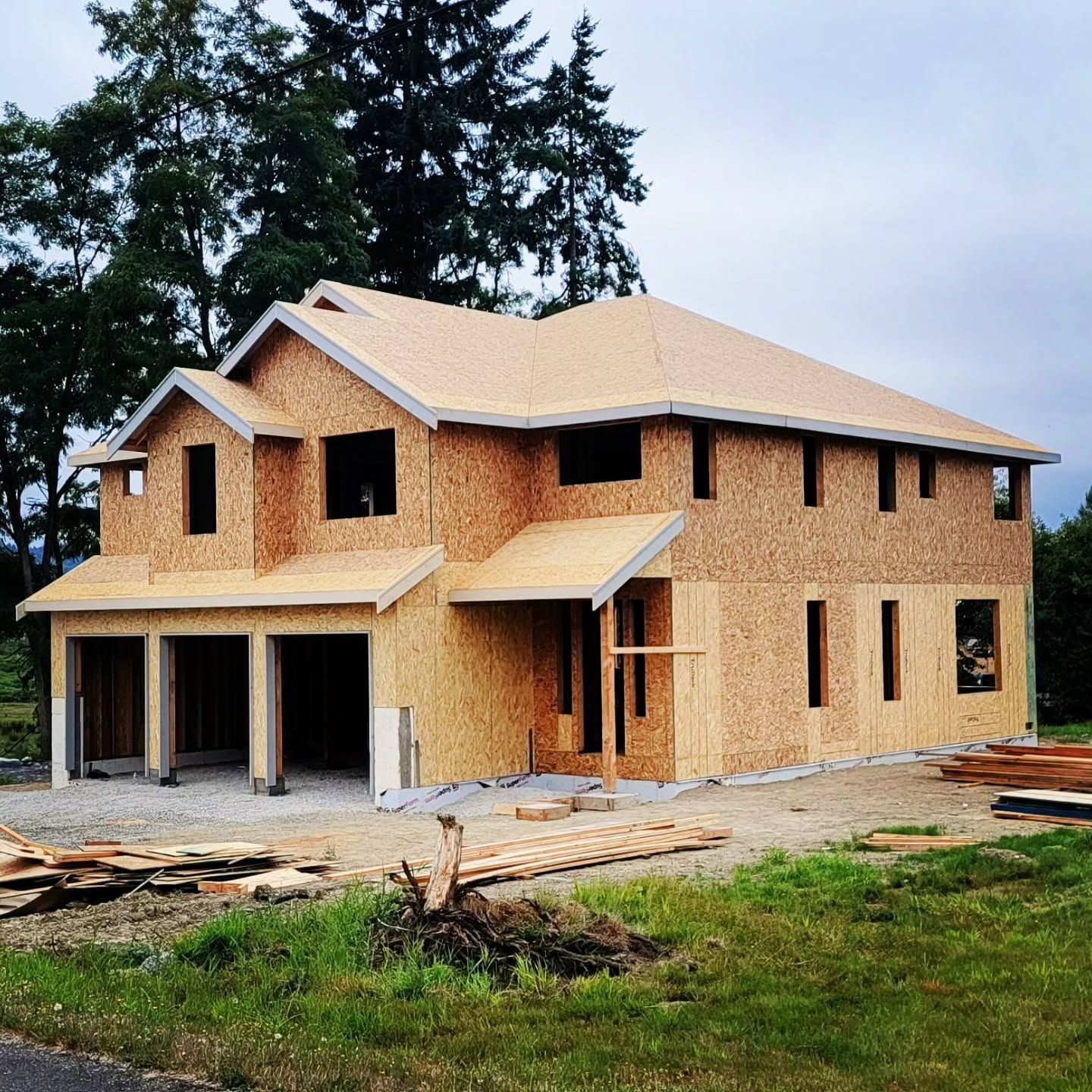 Two-story house under construction, with exposed wood framing and a two-car garage.