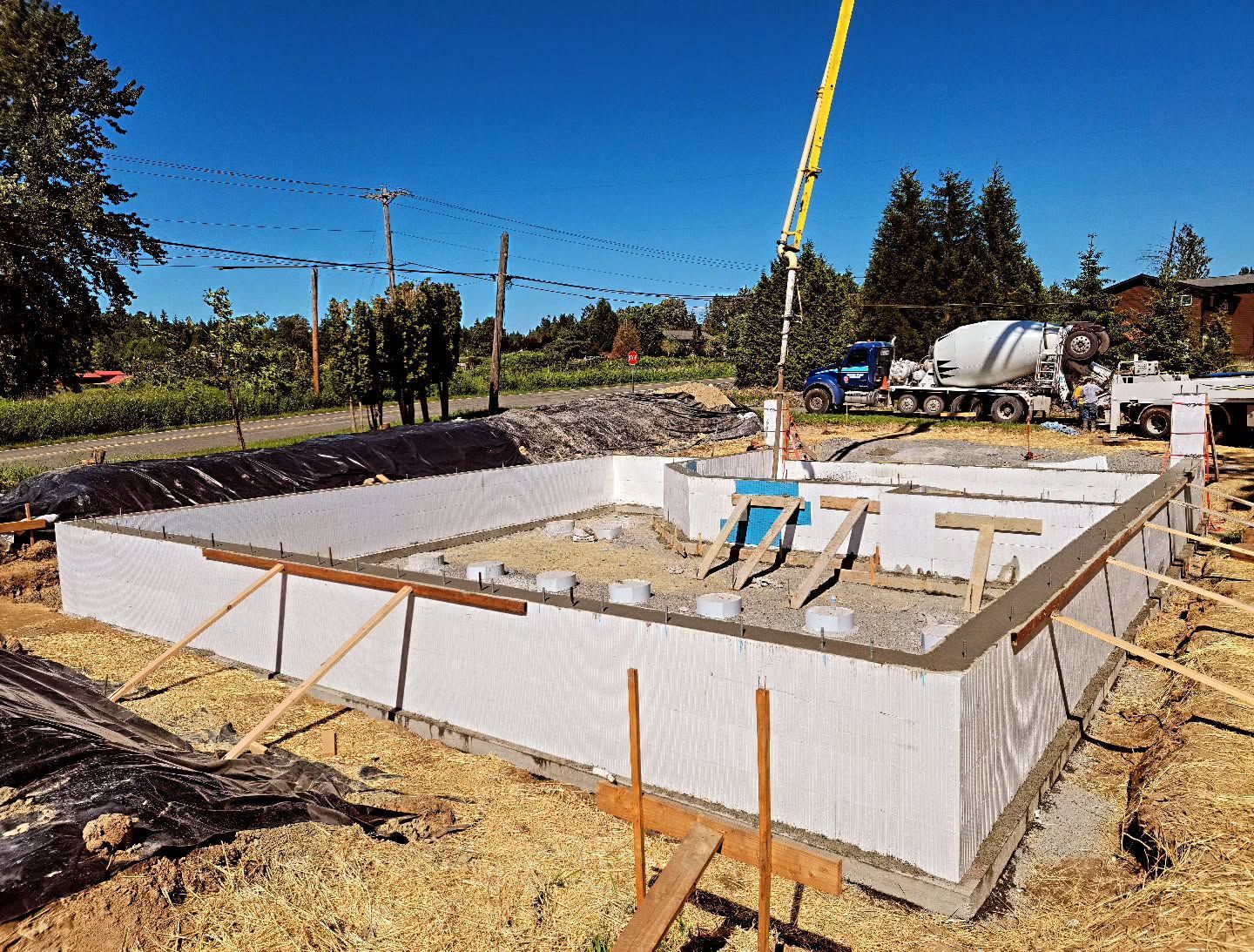 Foundation construction site with concrete being pumped; blue sky, trees.