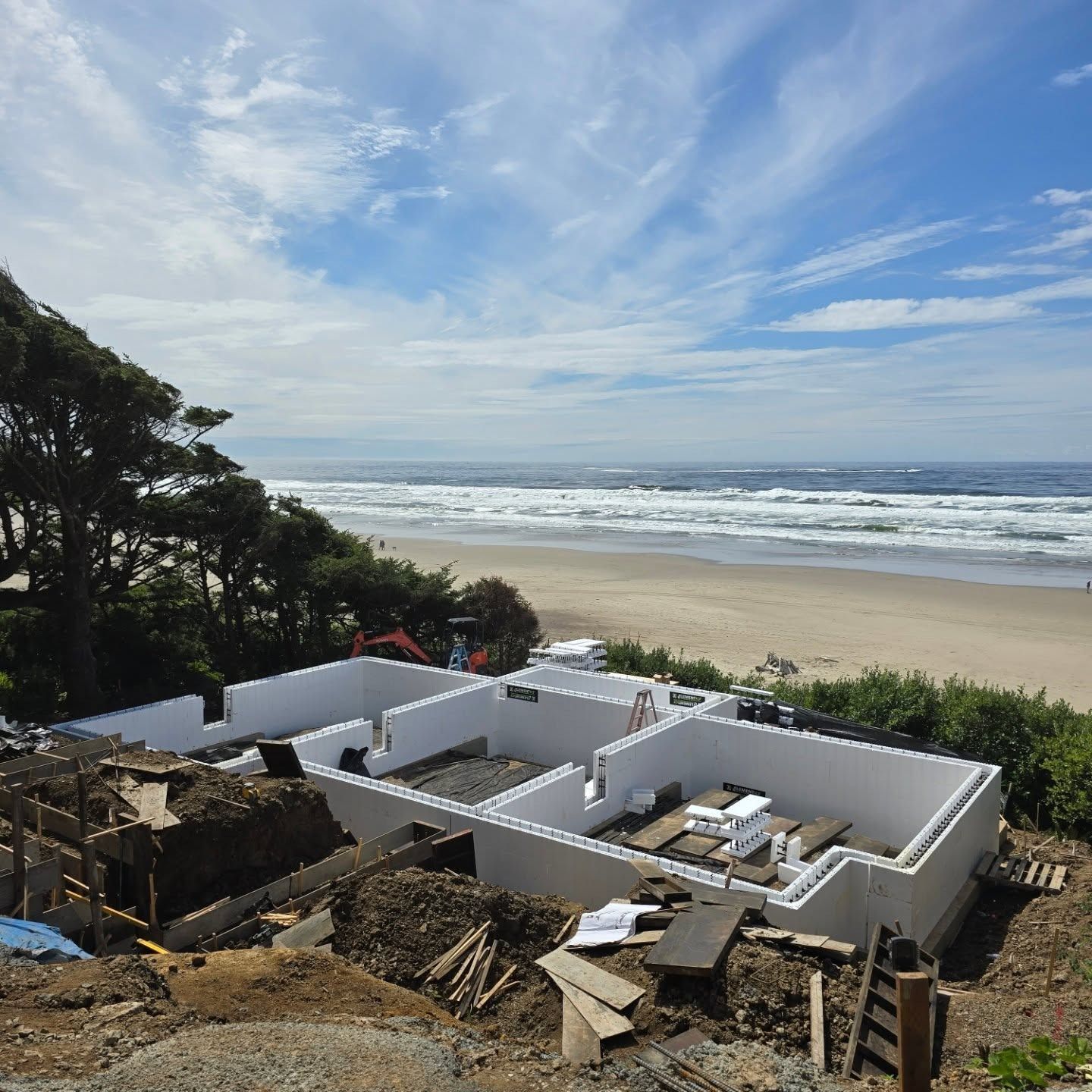 Foundation of a house under construction near the ocean. White walls, beach and sky in background.