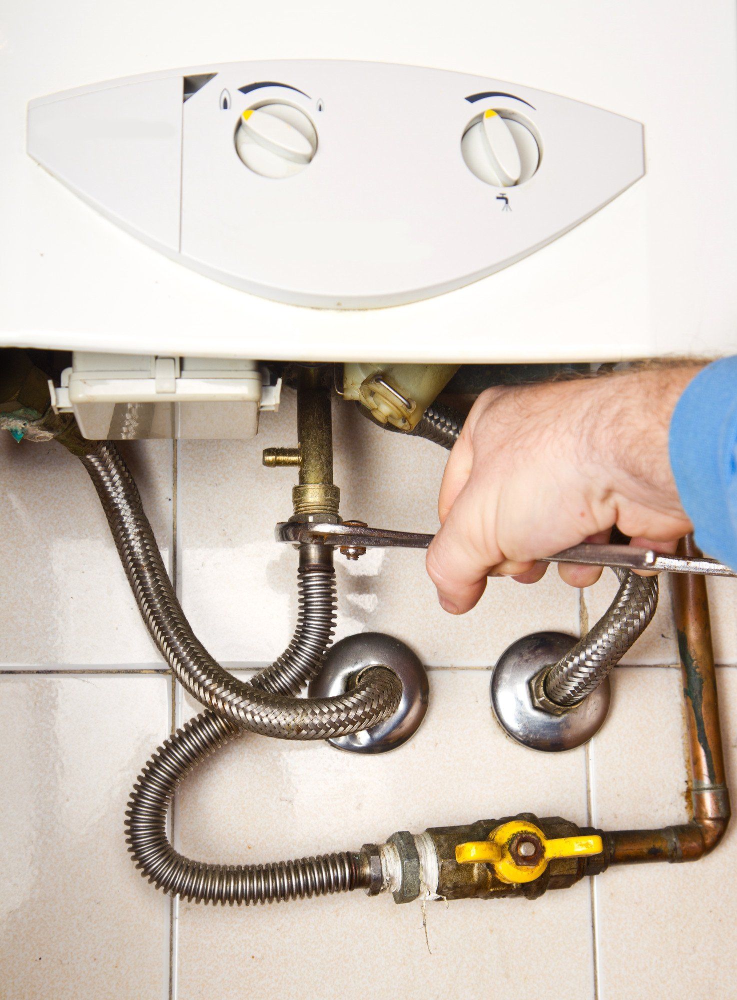 A technician uses locking pliers to tighten a copper pipe fitting on a wall-mounted boiler unit.