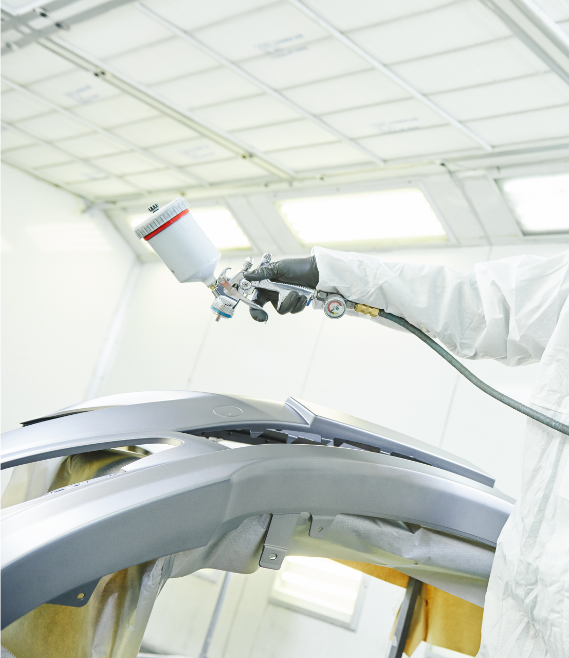 A man in a protective suit is spray painting a car bumper.
