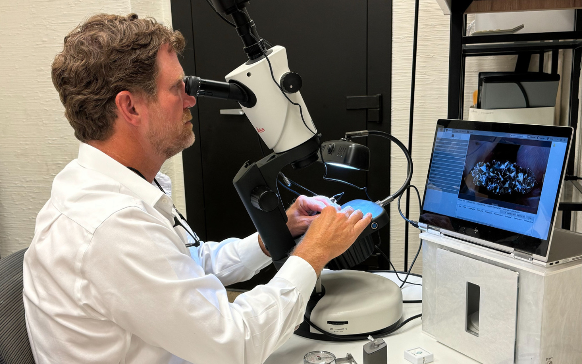 Man using a microscope, looking at a sample, with a laptop displaying the magnified view.