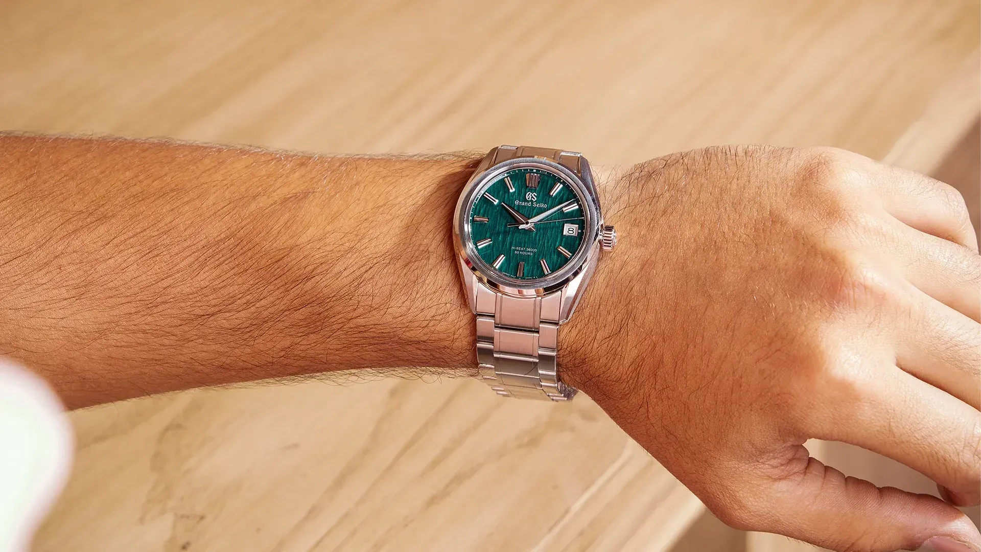 Person's wrist with a stainless steel watch with a green dial.