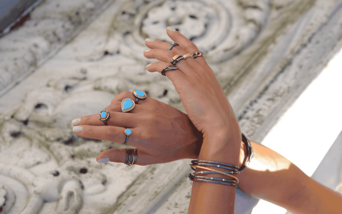 Hands adorned with turquoise rings and bracelets, posed against a textured white background.