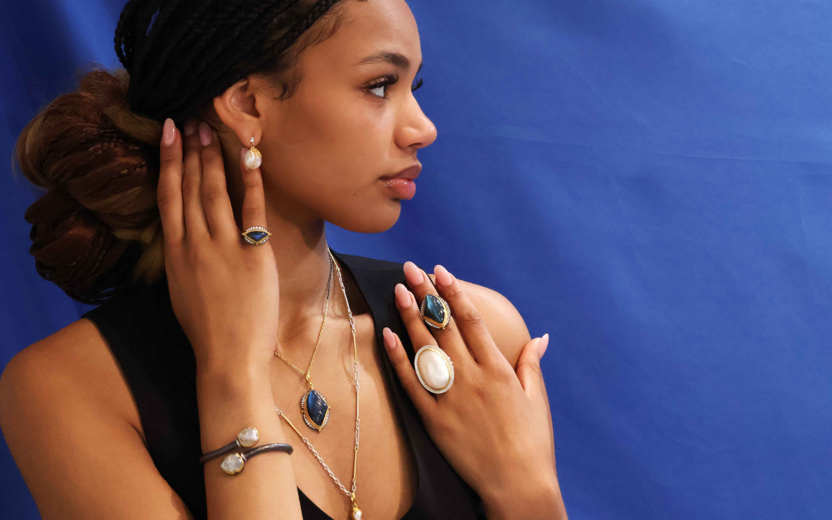 Woman with jewelry, including rings, earrings, and necklace, against a blue background.