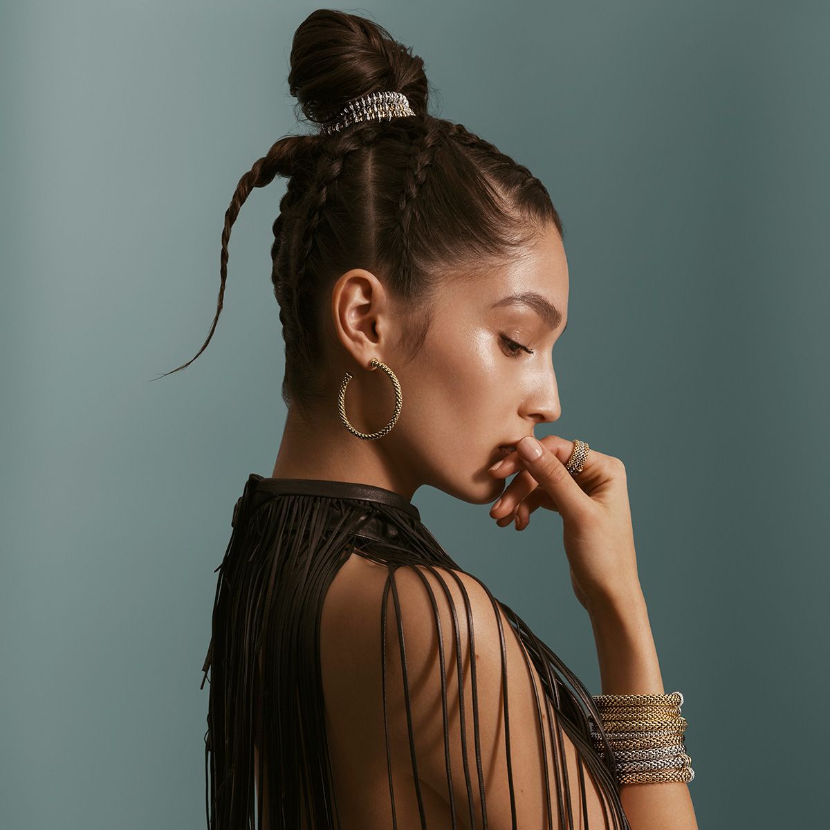 Woman with braided updo and hoop earrings, hand near mouth, against a blue background.