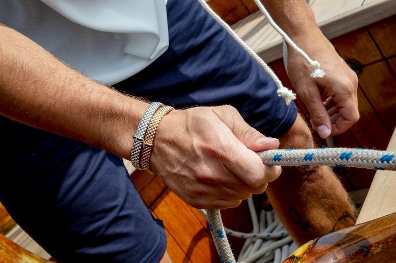Person in blue shorts holding a nautical rope, wearing two gold bracelets.