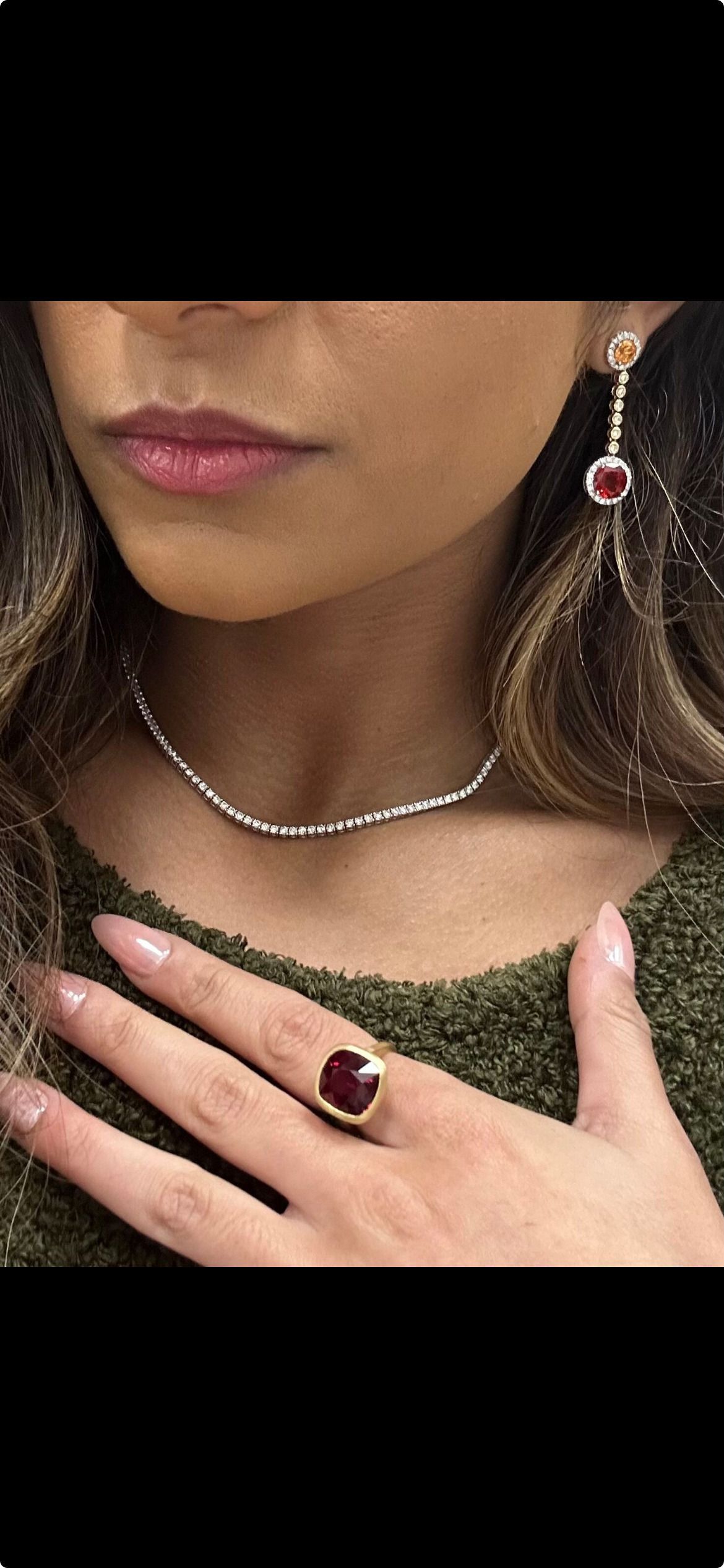 Woman wearing jewelry: necklace, earrings, and ring with a dark red stone.