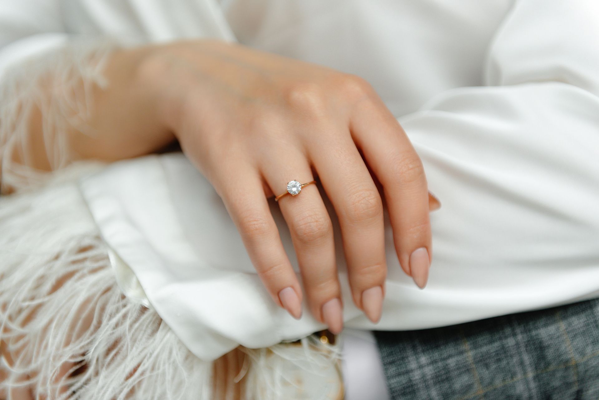 Hand with engagement ring, resting on white robe with feathers.