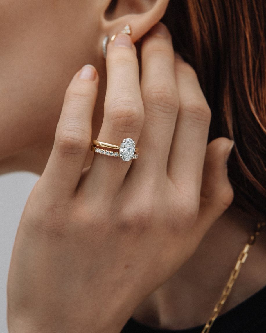 Hand wearing two rings, an engagement ring with an oval diamond and a band with tiny gems.