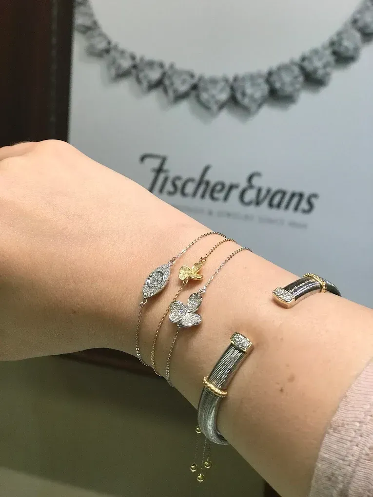 Wrist with diamond bracelets, Fischer Evans jewelry store display in background.