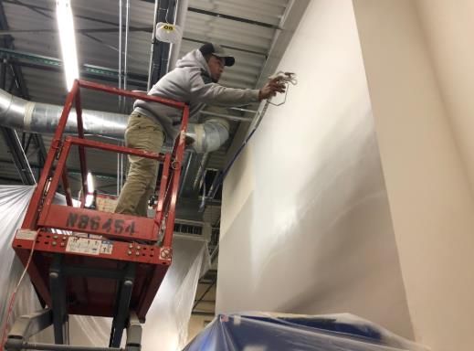 A man is standing on a scissor lift working on a wall.