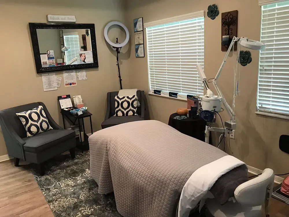 Aesthetic treatment room with bed, chairs, mirror, and equipment, in neutral colors.