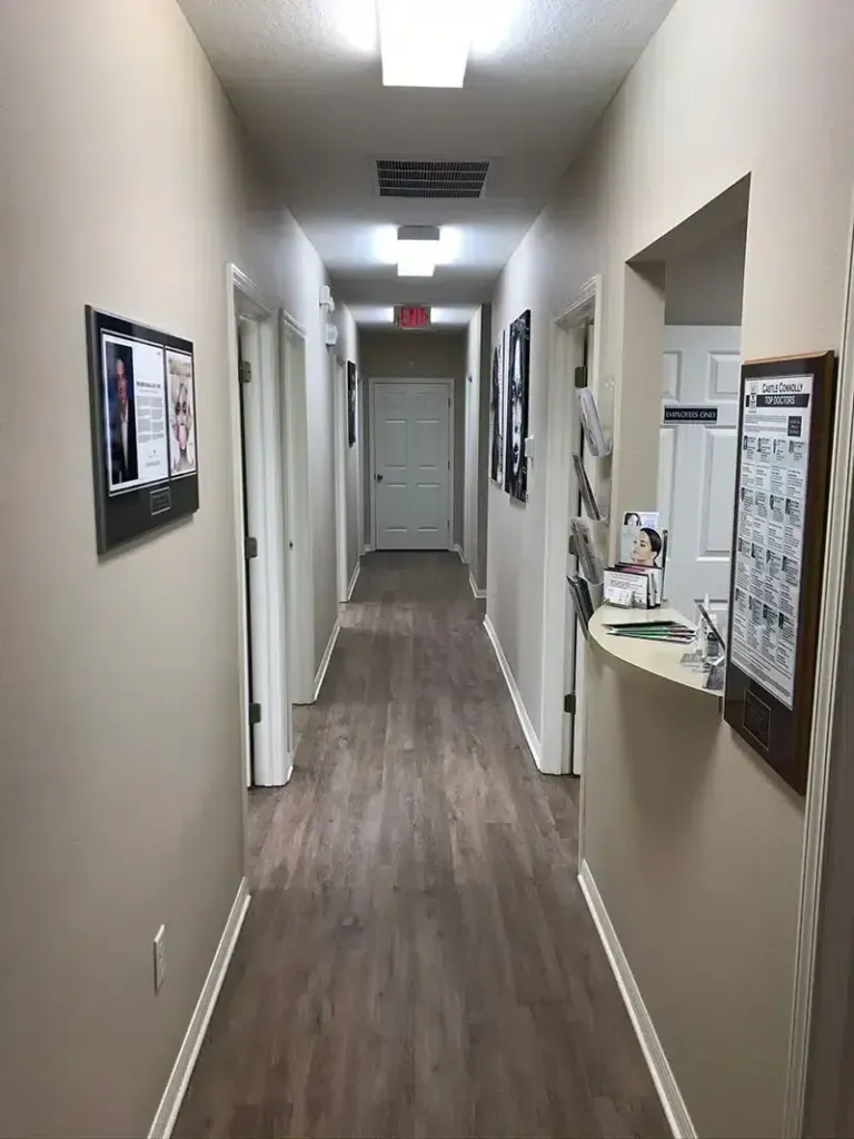 Hallway in a medical office with light brown walls and wood-look flooring. Doors line both sides.