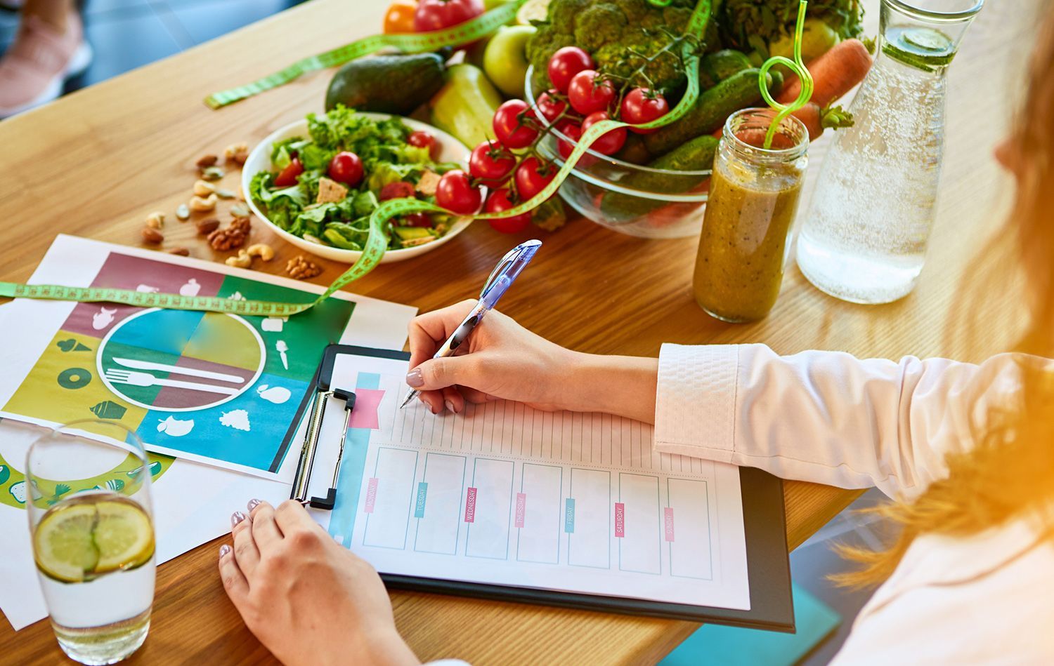 Woman writing on clipboard with healthy food and drinks on table. Woman writing on clipboard with healthy food and drinks on table.