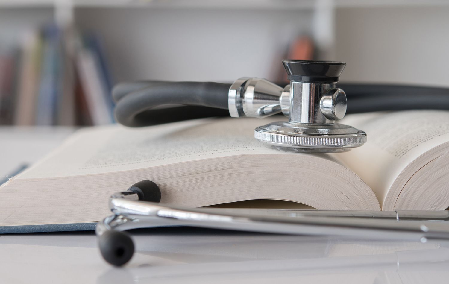 Stethoscope resting on an open book, possibly a medical textbook, on a desk.