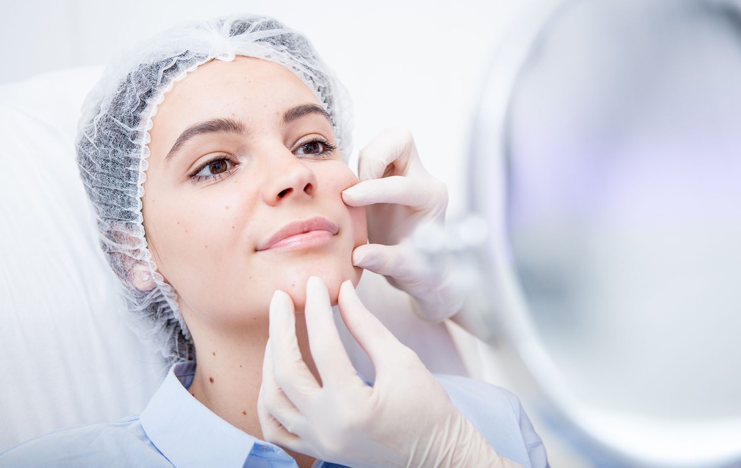 Woman having a cosmetic procedure on her face, being examined by gloved hands in a medical setting. Woman having a cosmetic procedure on her face, being examined by gloved hands in a medical setting.