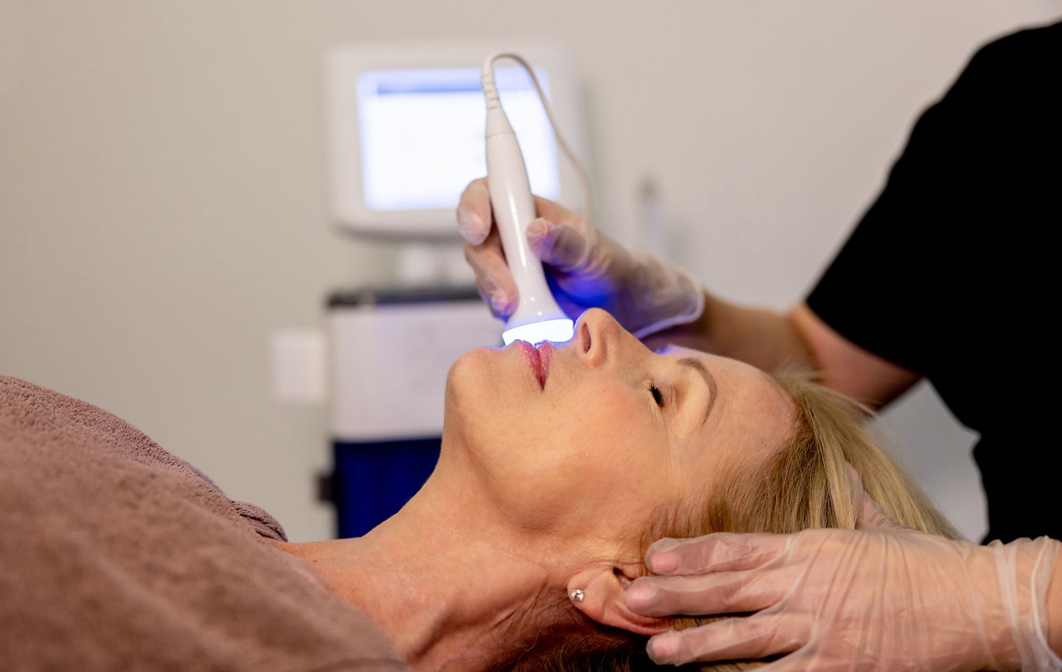 Woman receiving a skin treatment with a blue-light device. Woman receiving a skin treatment with a blue-light device.