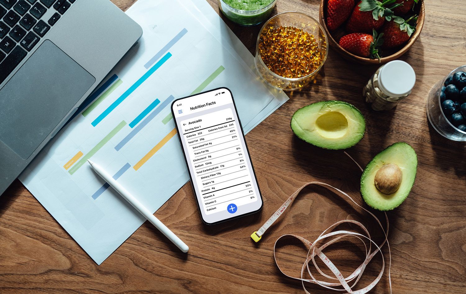 Laptop, phone with data, healthy foods, measuring tape on wooden desk; wellness concept.