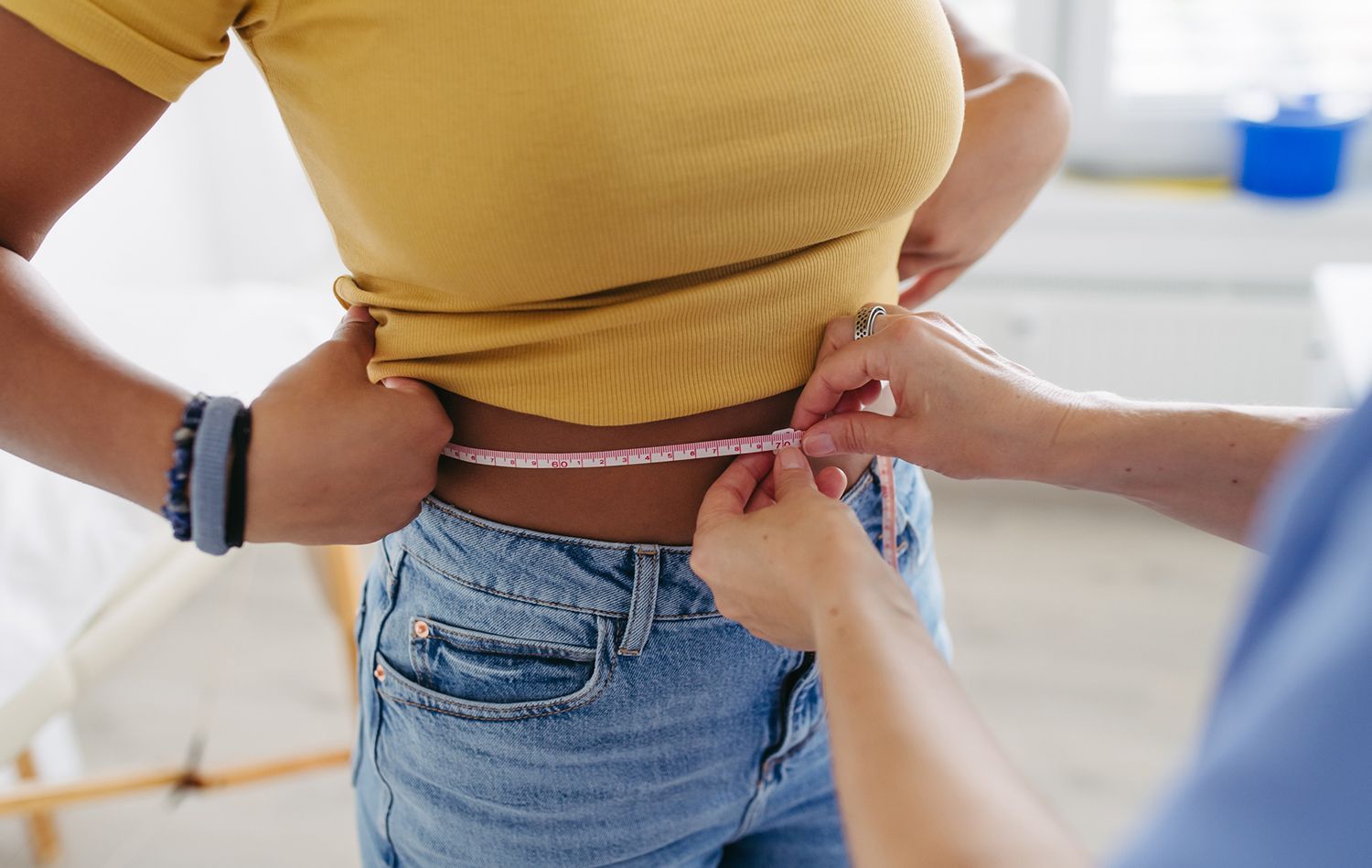 Person's waist being measured with a pink measuring tape by another person.