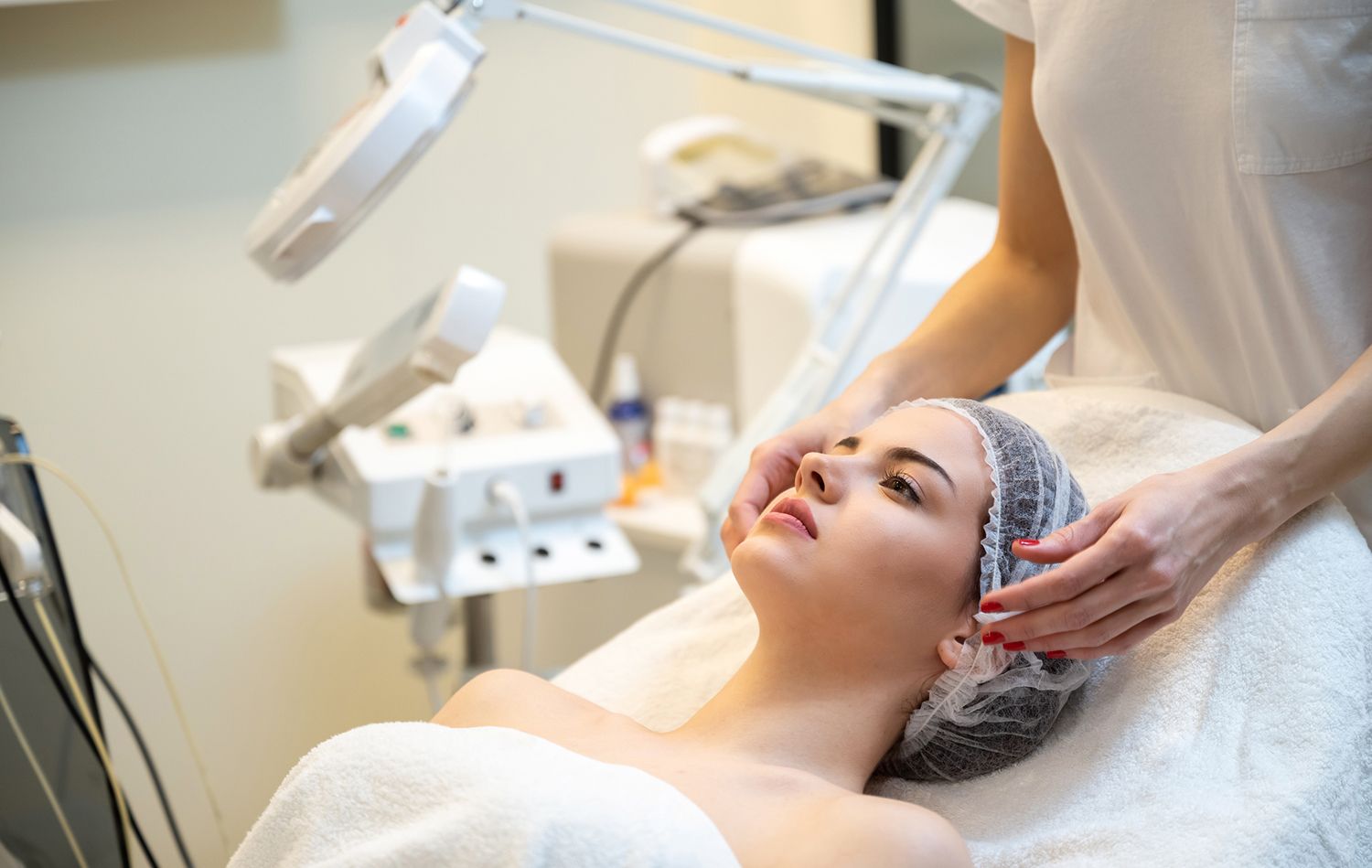 Woman receiving facial treatment at a spa. Therapist's hands on her face. Bright light and white setting. Woman receiving facial treatment at a spa. Therapist's hands on her face. Bright light and white setting.