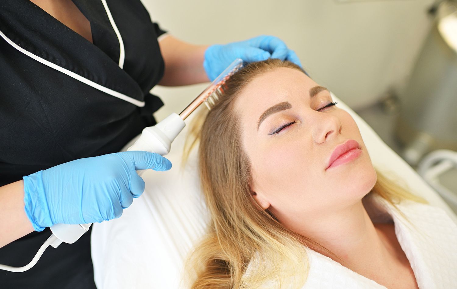 Woman receiving high frequency hair treatment; technician holds wand to her scalp. Woman receiving high frequency hair treatment; technician holds wand to her scalp.
