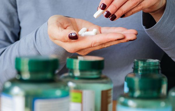 Woman holding white pills in her hand, taking medication from a bottle.