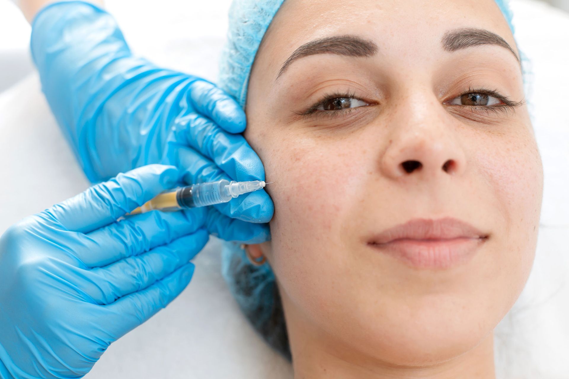 Woman receiving a facial injection in a medical setting, wearing a surgical cap. Woman receiving a facial injection in a medical setting, wearing a surgical cap.