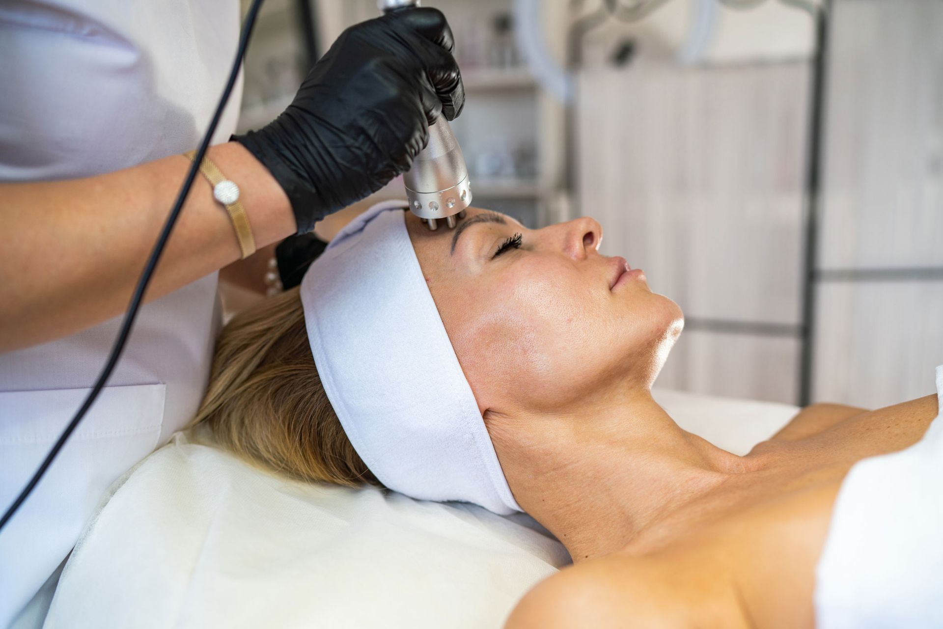 Woman receiving facial treatment in a spa, using a handheld device on her forehead.